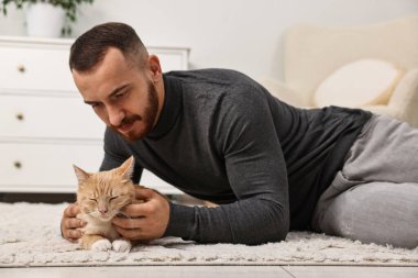 Evdeki sevimli kızıl kediyi okşayan adam.