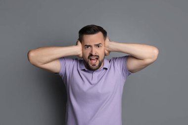 Gri arka planda kulaklarını kapatan adam.