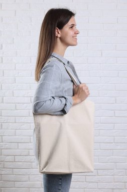 Beyaz tuğla duvarın yanında boş alışveriş torbası olan bir kadın. Tasarım için model