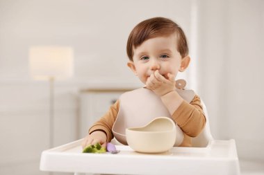 Evdeki yüksek sandalyede sağlıklı yiyecekler yiyen şirin bir bebek.