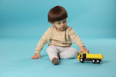 Açık mavi arka planda oyuncak kamyonla oynayan şirin bir çocuk.