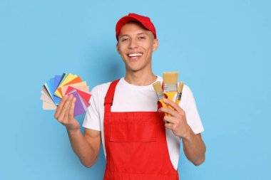 Açık mavi arkaplanda renk paletleri ve fırçaları olan genç dekoratörün portresi