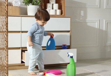 Küçük çocuk dolapta deterjan şişesiyle oynuyor, mesaj için yer var. Çocuk tehlikede.