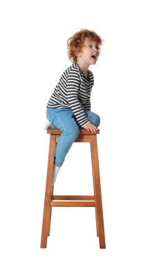 Küçük çocuk beyaz arka planda taburede oturuyor.