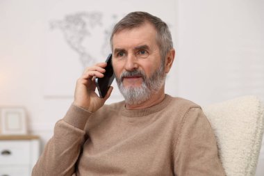 Evde akıllı telefondan konuşan olgun bir adam.