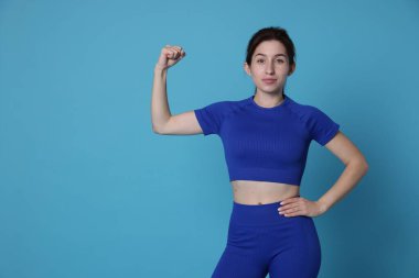 Spor kıyafetli bir kadın açık mavi arka planda pazılarını gösteriyor. Mesaj için yer var.