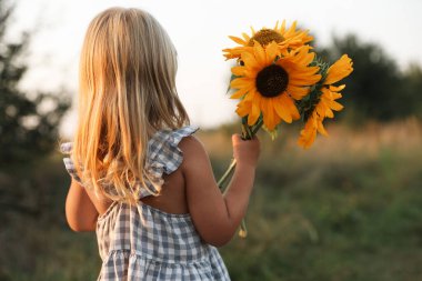 Meadow 'da ayçiçekleri olan küçük bir kız. Çocuk güzel doğanın tadını çıkarıyor
