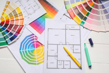 Renk paletleri, yer planları ve beyaz ahşap masa üzerindeki kırtasiyeli tasarımcı işyeri.