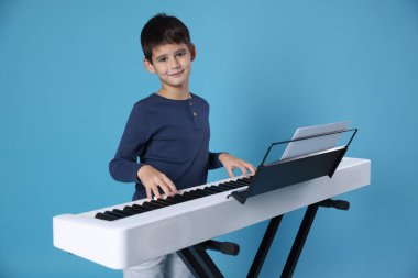 Açık mavi arka planda sentezleyici oynayan sevimli çocuk.
