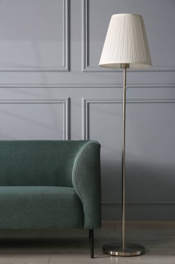 Gri duvarın yanında rahat bir kanepe ve lamba.