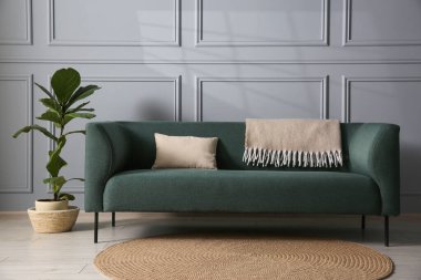 Gri duvarın yanında rahat bir kanepe ve çiçek var.