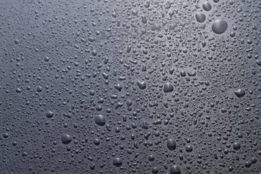 Su damlaları gri cam yüzeyde, üst manzarada.