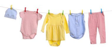 Different baby clothes drying on laundry line against white background