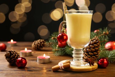 Lezzetli Noel kokteyli (eggnog) cam, şenlikli dekor ve ahşap masada yanan mumlar.