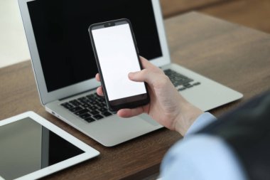 İş adamı, bilgisayarın yanında akıllı telefon ve kapalı bir masadaki tablet kullanıyor. Modern teknoloji