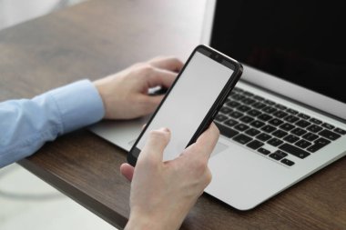 İş adamı, kapalı bir masadaki bilgisayarın yanında akıllı telefon kullanıyor, yakın plan. Modern teknoloji