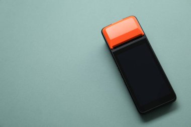 Soluk turkuaz arka planda bir ödeme terminali, üst manzara. Metin için boşluk