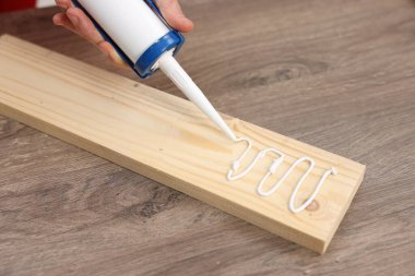 Man with caulking gun glueing wooden plank at table, closeup clipart