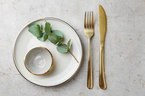 Güzel tabak, sos kasesi, altın çatal bıçak takımı ve okaliptüs dalı gri desenli masa, düz uzanmış.