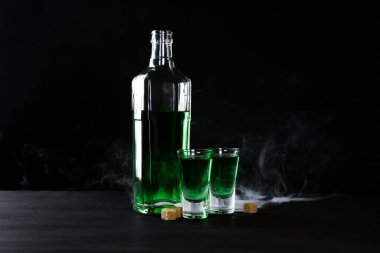 Absinthe shot bardakları, şişe ve esmer şeker siyah arka planda dumanlı
