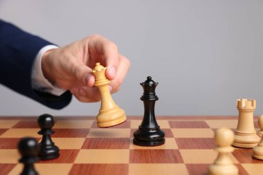 Satranç tahtasında açık gri arka planda satranç oynayan iş adamı, yakın plan. Rekabet konsepti