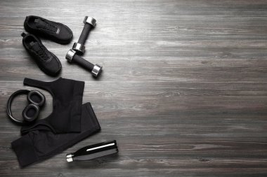 Siyah spor kıyafetleri ve tahta arka planda spor ayakkabıları olan düz kompozisyon, metin için boşluk