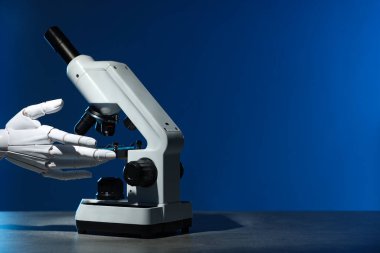 Yapay zeka. Mavi arkaplanda mikroskopla çalışan robot el, metin için boşluk