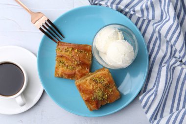 Lezzetli baklava, doğranmış fındık, bir kaşık dondurma ve beyaz masada kahve.