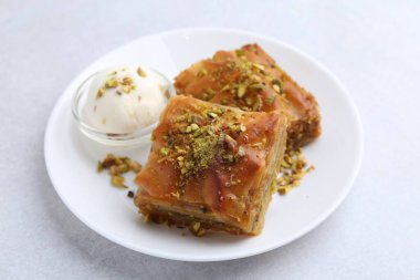 Lezzetli baklava, doğranmış fındık ve açık gri masada bir kepçe dondurma, yakın plan.