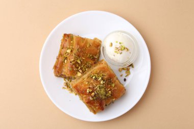 Lezzetli baklava, doğranmış fındık ve bir kepçe dondurma, bej masa, üst manzara.
