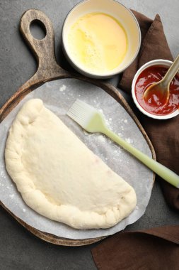 Pişmemiş calzone pizza, sos ve yumurta sarısı gri masada, düz yerde.