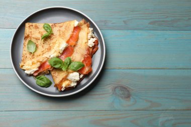 Somonlu leziz krepler, krem peynirli fesleğen ve açık mavi ahşap masa, üst manzara. Metin için boşluk