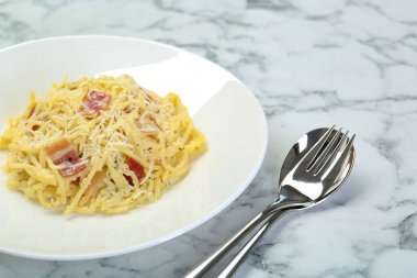 Beyaz mermer masada servis edilen domuz pastırmalı lezzetli makarna, yakın plan.