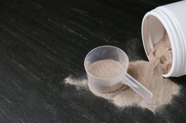 Koyu dokulu masa üzerinde protein tozu ile kavanoz ve kepçe, metin için boşluk