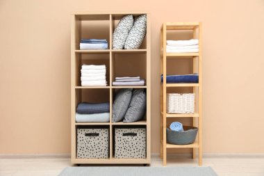 Ev yapımı tekstil organizasyonu. Bej duvarın yanındaki raflarda farklı yastıklar, çarşaflar ve battaniyeler var.