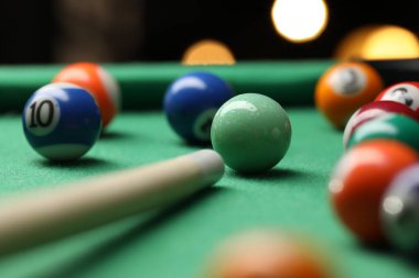 Many colorful billiard balls and cue on green table indoors, closeup