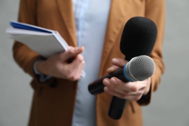Gri arka planda mikrofon ve not defteri olan gazeteci, yakın plan