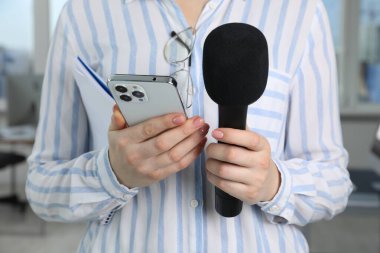 Kapalı mekanda mikrofon, defter ve akıllı telefonu olan bir gazeteci.