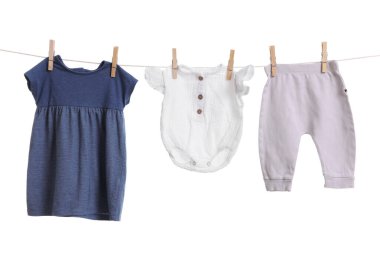 Different baby clothes drying on laundry line against white background