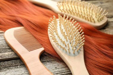 Farklı fırçalar, taraklar ve bir tutam saç ahşap masada, yakın plan.