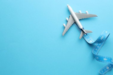 Plane model and measuring tape as flight path on light blue background, top view. Space for text clipart