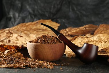 Tütün, kurumuş yapraklar ve siyah masada tüttürme piposu. Yakın plan.