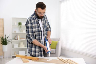 Man with caulking gun glueing plywood indoors clipart