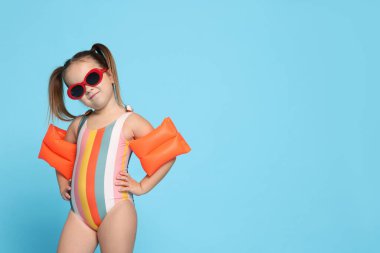 Açık mavi arka planda yüzme kolluklu mayo giymiş şirin küçük bir kız. Metin için boşluk