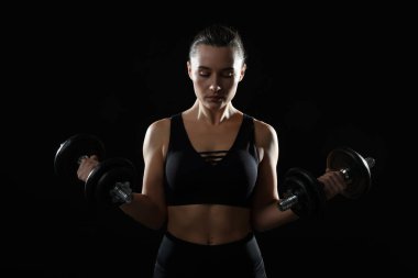 Spor giyinen güzel bir kadın, siyah arka planda halterleri olan.