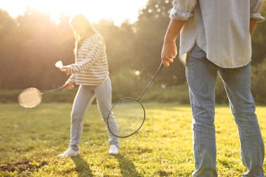 Güneşli bir günde parkta badminton oynayan genç bir kadın ve erkek.