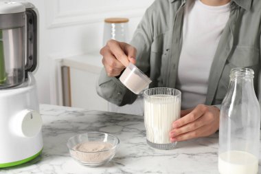 Protein kokteyli yapıyorum. Beyaz mermer masada sütlü bardağa toz ekleyen kadın, yakın plan.