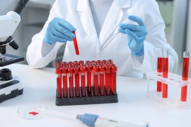 Laboratuvar testi. Doktor, kan örneği ve pipetle test tüpünü kapalı bir masada tutuyor.