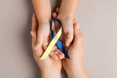 Koyu bej arka planda sarı ve mavi kurdeleli çocuklu bir kadın. Down sendromu farkındalığı