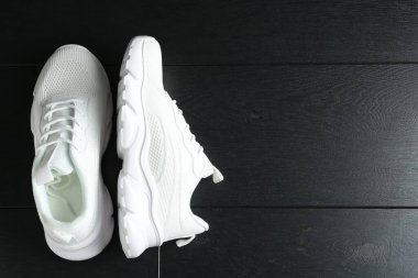 Siyah ahşap arka planda bir çift şık beyaz spor ayakkabı. Metin için boşluk